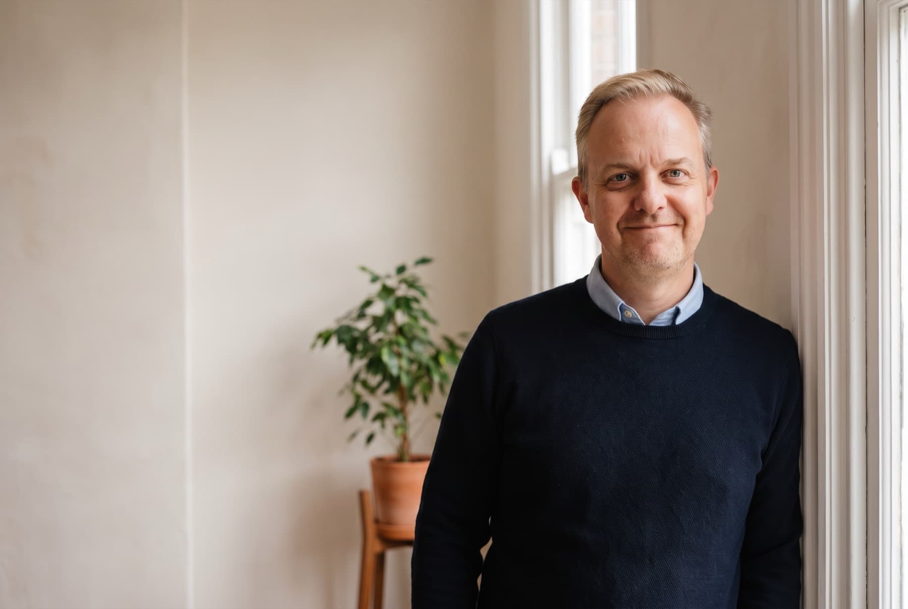Mark Craig standing by a window in his counselling room, smiling.